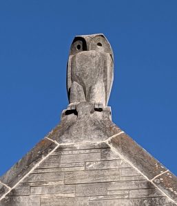 A stone owl perched on the top of a roof.