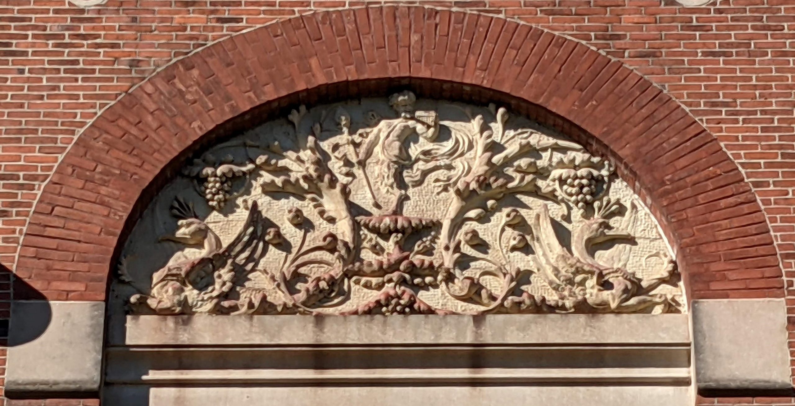 A carving of Bacchus among grapes and peacocks on the side of a building.