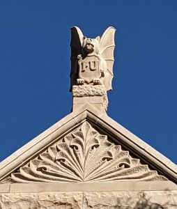 A stone carving of a bat holding a shield atop a roof.