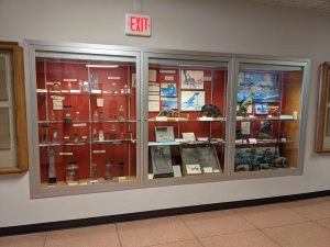 Photo of a display case in a hallway. The case is filled with specimens in jars and dinosaur models.