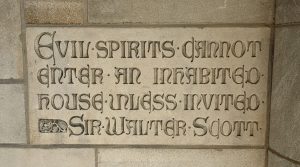Carving of the words "Evil spirits cannot enter an inhabited house unless invited - Sir Walter Scott".