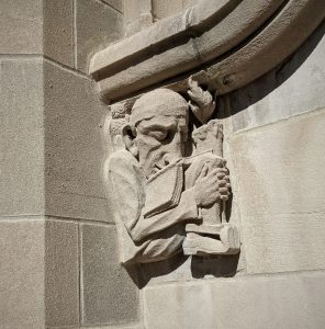 Carving of a sleeping student hunched over a textbook with an owl perched on his shoulder.