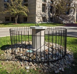 Image of a limestone sundial surrounded by a wrought-iron fence.