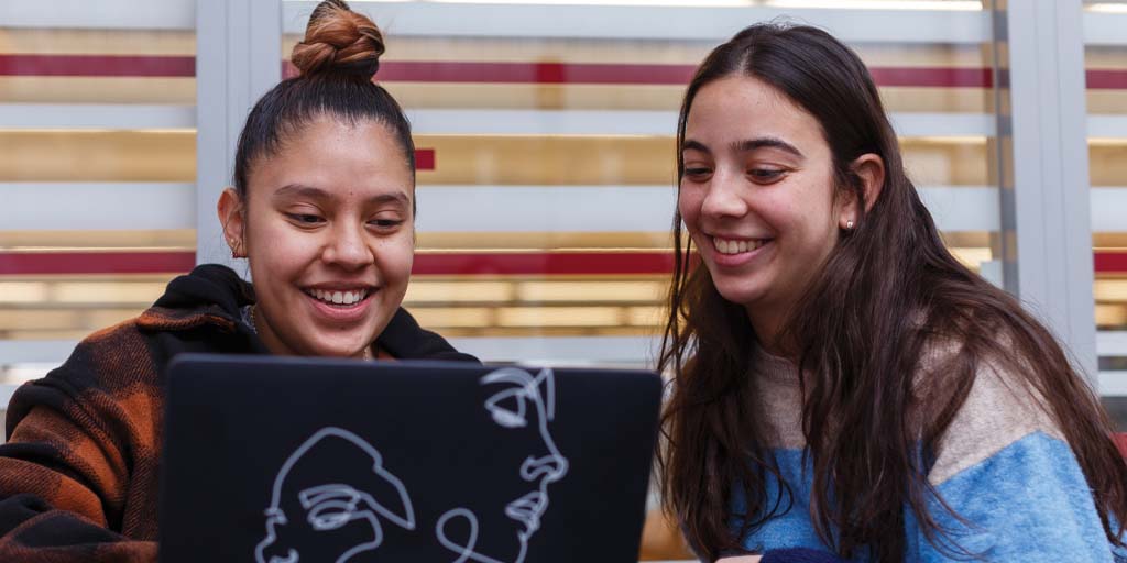 Two young women look at the screen of a laptop computer.