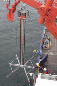 Photo showing several crew members lowering large vibra corer from the ship deck to the sea floor.