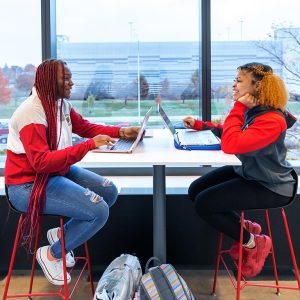 Two students sit at a table with laptops