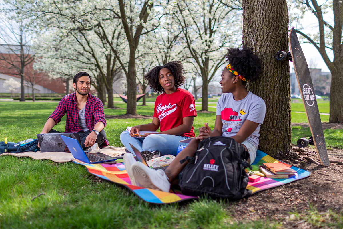 Three students sitting under a tree on campus.