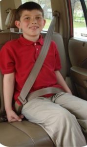 A child sitting in the back seat of a vehicle strapped in a seat belt