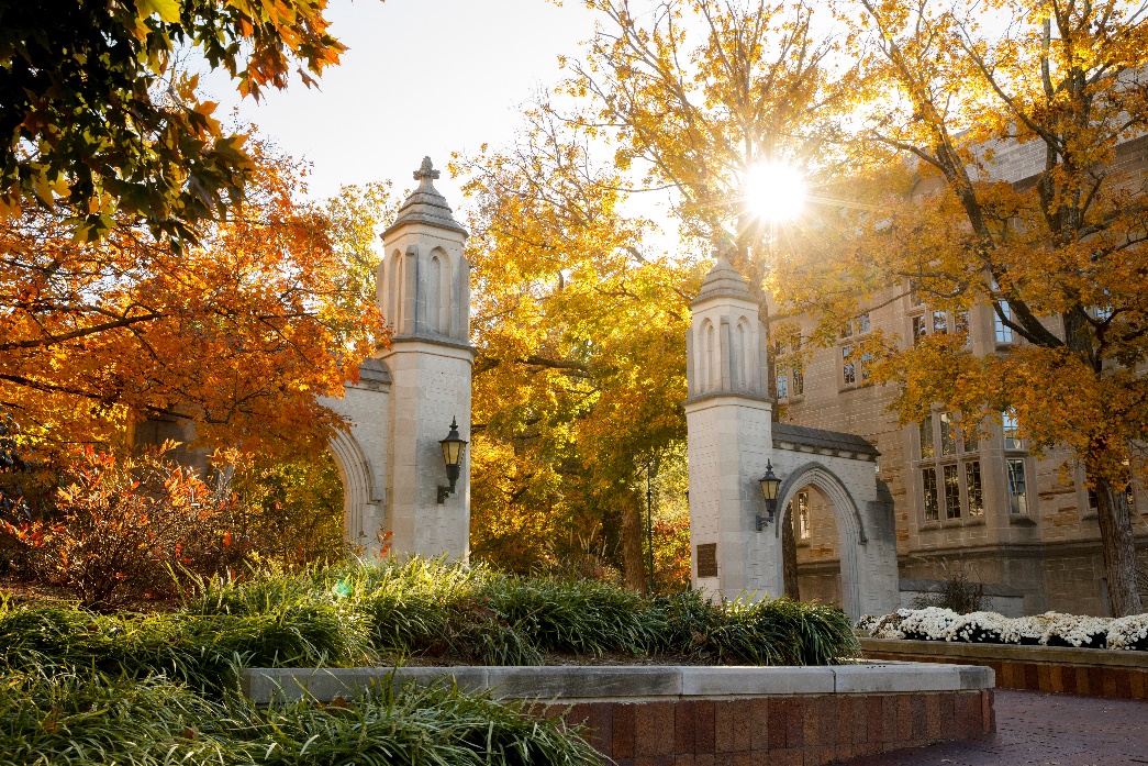 The Sample Gates at Indiana University surrounded by fall foliage with the sun shining through.