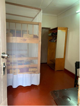 A bedroom with one bunkbed on the left covered by a mosquito net and a wardrobe on the right. Part of a table and chair can be seen in the bottom right