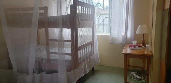 A room with one bunk bed to the left that is covered by a mosquito net and a side table with a lamp to the right.