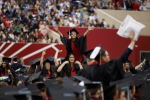 A graduate sits on a friend’s shoulders to wave to friends and family in the stands during the IU Bloomington Undergraduate Commencement at Memorial Stadium.