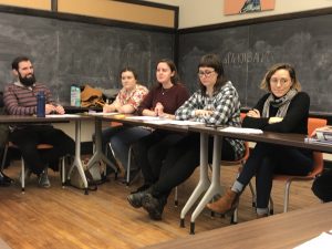 4 people are seated at a rectangular table in room with black chalkboards on the wall.