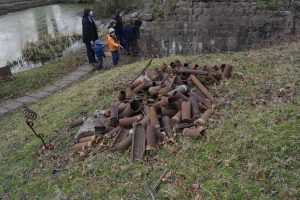 A pile of rusted shells in the foreground and visitors in the background walking on a path along the folloded crate hole.