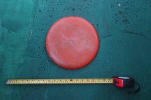 Object 4 Reddish orange round plastic frisbee. About 9 inches in diameter. Frisbee contains the logo Mall del Sol