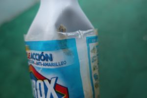 white plastic Clorox bottle about 8.5 inches tall. Clorox label still present, writing is visible, discernable, and in Spanish. Close up of a stain or a growth on bottle.