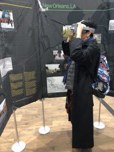 A woman wearing a VR headset stands looks at an exhibit with images and text printed on a black fabric.