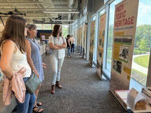 Three individuals looking at a poster display for Indy Toxic Heritage exhibition