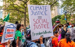 photo of crowd protesting with a prominent handheld sign reading "Climate Justice = Social Justice Freedom to Breathe"