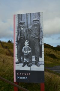 outdoor exhibit panel with a photograph of two men in miners clothing with a young boy standing in front of them.