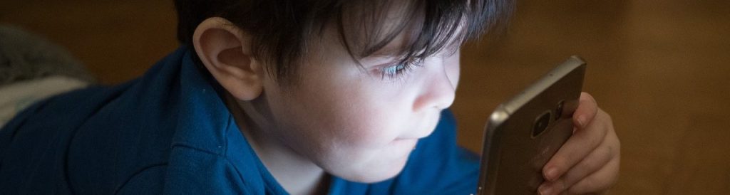 The glow of a smartphone shines on a young child's staring face