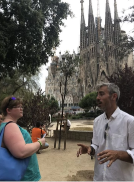 A photo of two people talking with a building in the background.