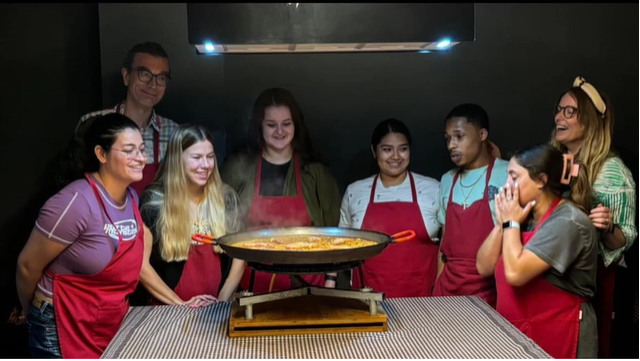 A photo of a group of people standing around a paella pan.