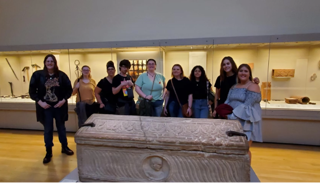 A photo of nine people posing with ancient artifacts.