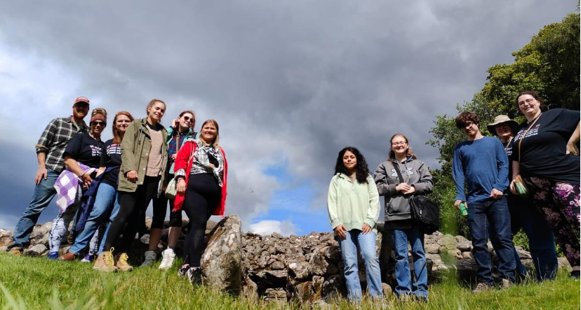 A photo of eleven people posing in front of ancient Scottish ruins.