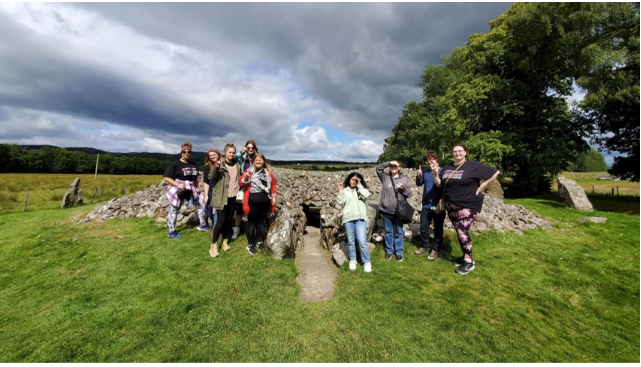 A photo of nine people posing in front of ancient Scottish ruins.