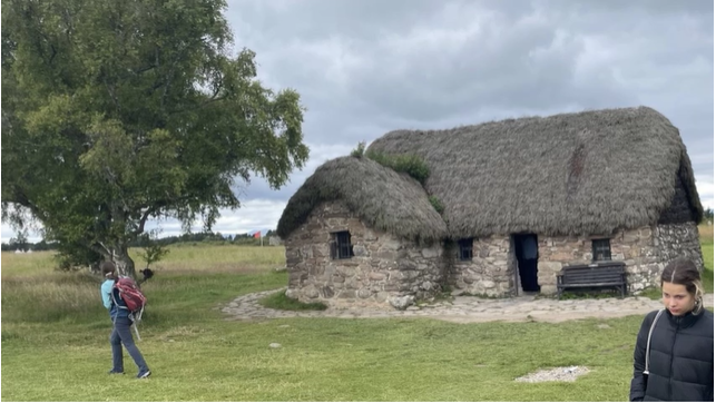 A photo of two people walking in front of an old Scottish cottage.