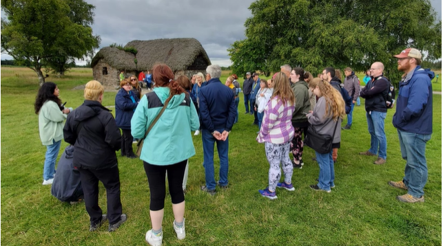 A photo of a large group of people listening to an educational talk in front of an old Scottish cottage.