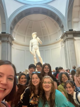 A photo of a group of people posing for a selfie in front of David of Michelangelo.