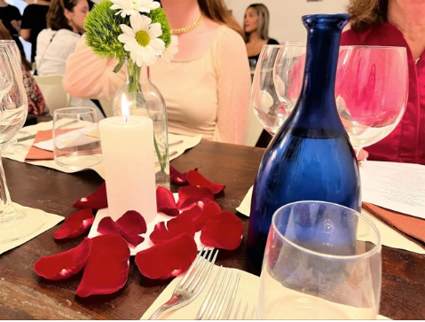 A photo of a candle with rose petals around it sitting on a table with glasses.