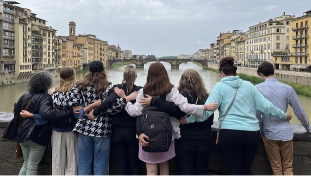 A photo of a group of people posing facing away from the camera on a bridge.