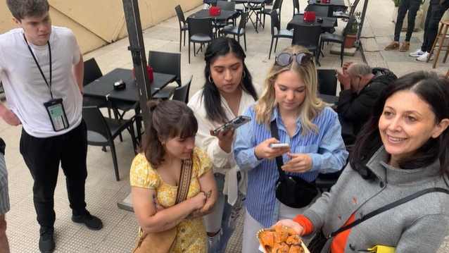 A photo of a group of people listening to a person speak.