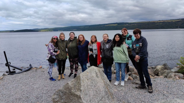 A photo of nine people standing in front of Loch Ness.