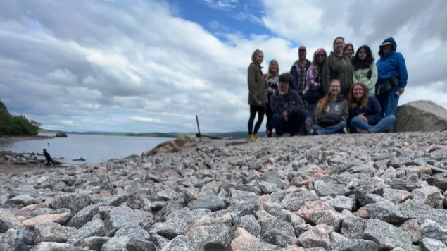 A photo of eleven people posed on rocks in front of Loch Ness.