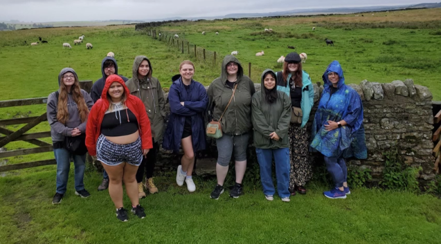 A photo of a group of nine people standing in front of a sheep pasture.