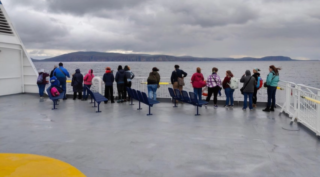 A photo of a group of people on the deck of a ferry.