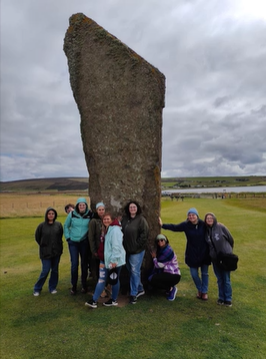 A photo of nine people posing in front of a standing stone.