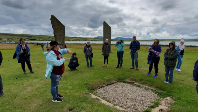 A photo of a group of people in a circle standing in a circle of standing stones.