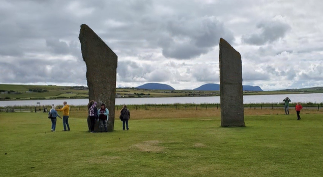 A photo of seven people in the distance examining a standing stone.