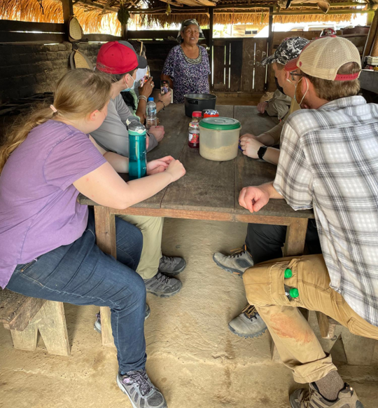 Image of a group of people sitting at a table listening to a person give a presentation.