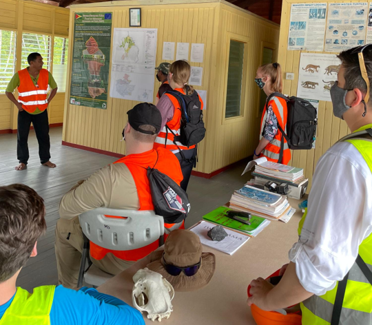 Image of a group of people listening to a person give a presentation.