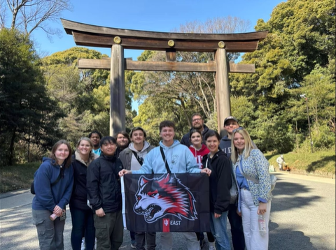 A photo of a group of people posing in front of a wooden Torii.