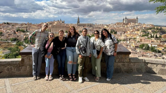 A photo of a group of people posing on a terrace with a city in the background.