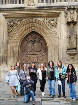 A photo of nine people posing in front of Bath Abbey.