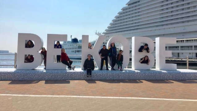 A photo of a group of people standing on a pier next to Japan's "Be Kobe" monument.