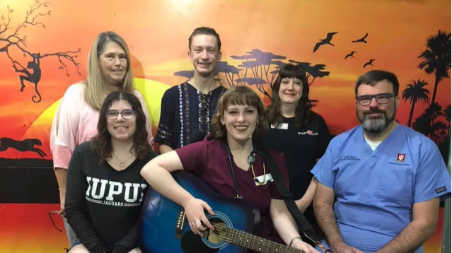 An up close photo of a group of people posing with a guitar.